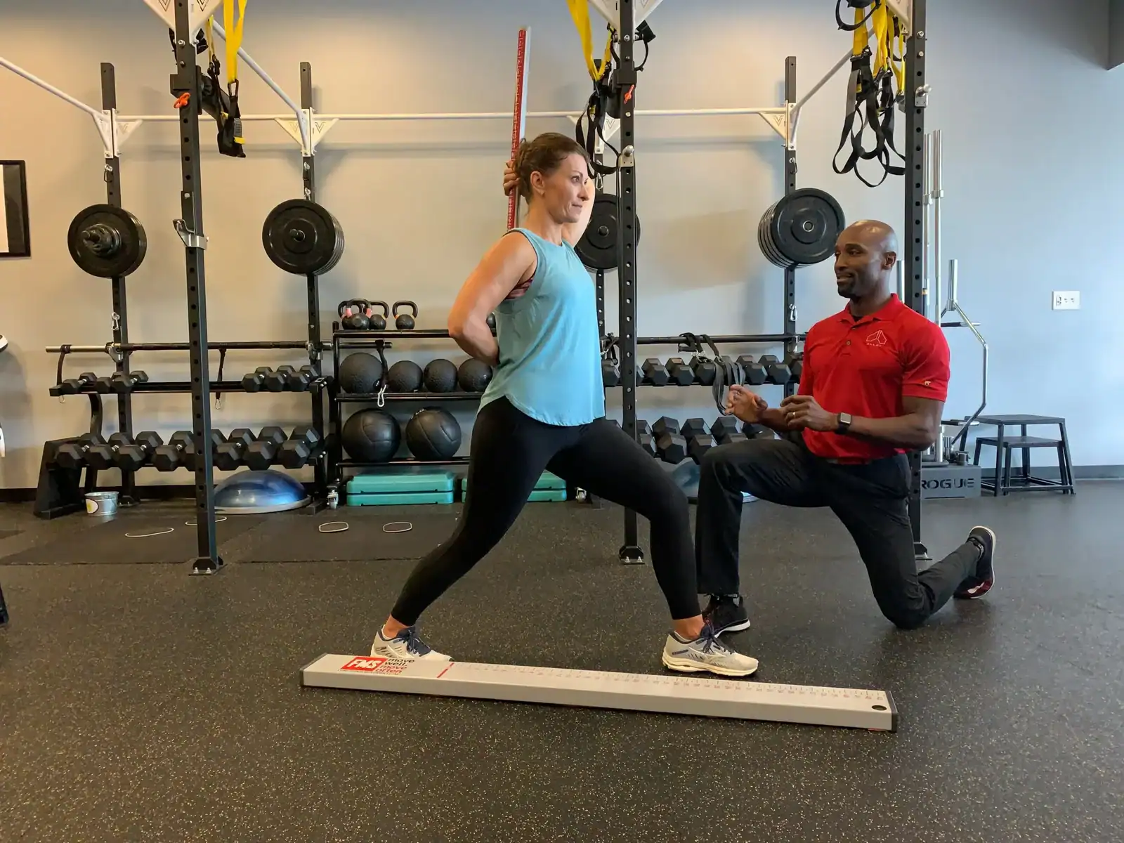 Woman performing a lunge exercise while a trainer observes in a gym setting