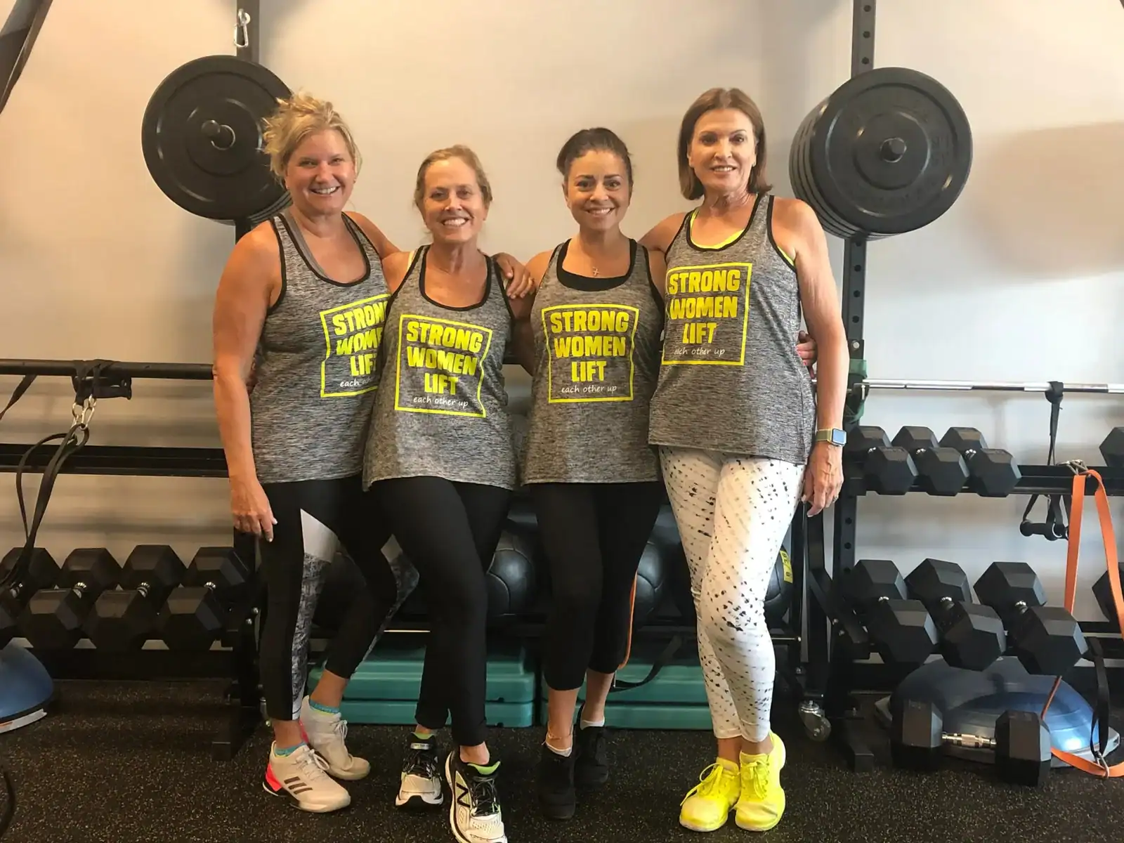 Four women in workout gear posing confidently in a gym setting