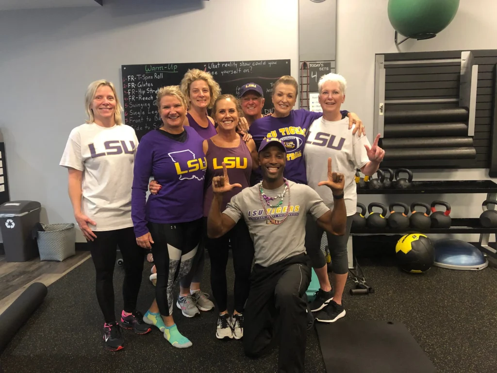 Group of eight people posing in athletic wear, smiling in a gym setting