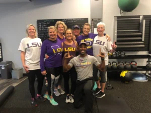 Group of eight people posing in athletic wear, smiling in a gym setting.