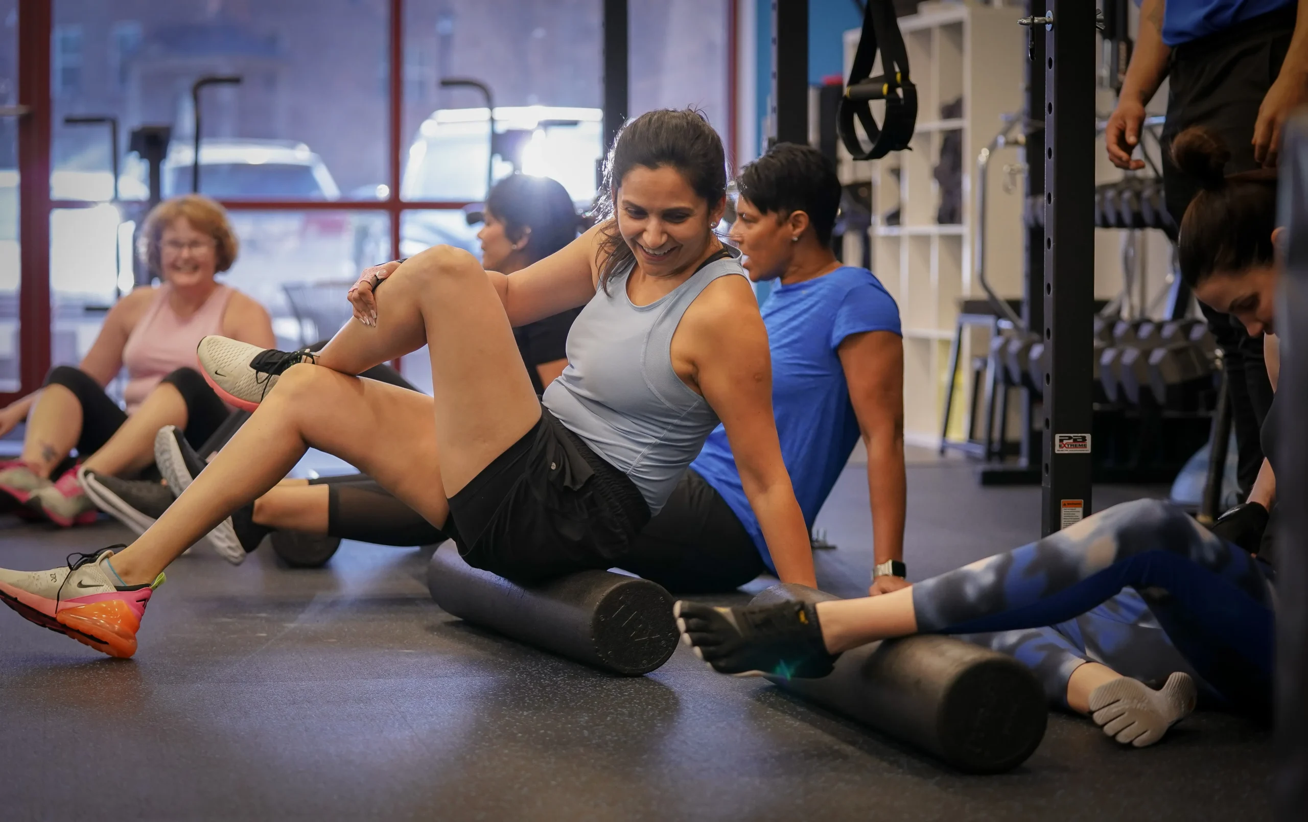 Group of people exercising on foam rollers in a gym setting.